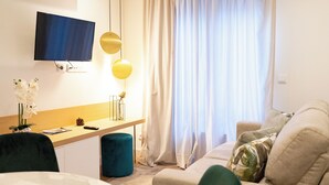 A modern hotel room with a flat-screen TV mounted on the wall, a desk with a remote control, a vase with flowers, and a sofa with cushions. - N&N Home Porto, your home in the center of Porto.  (Porto)