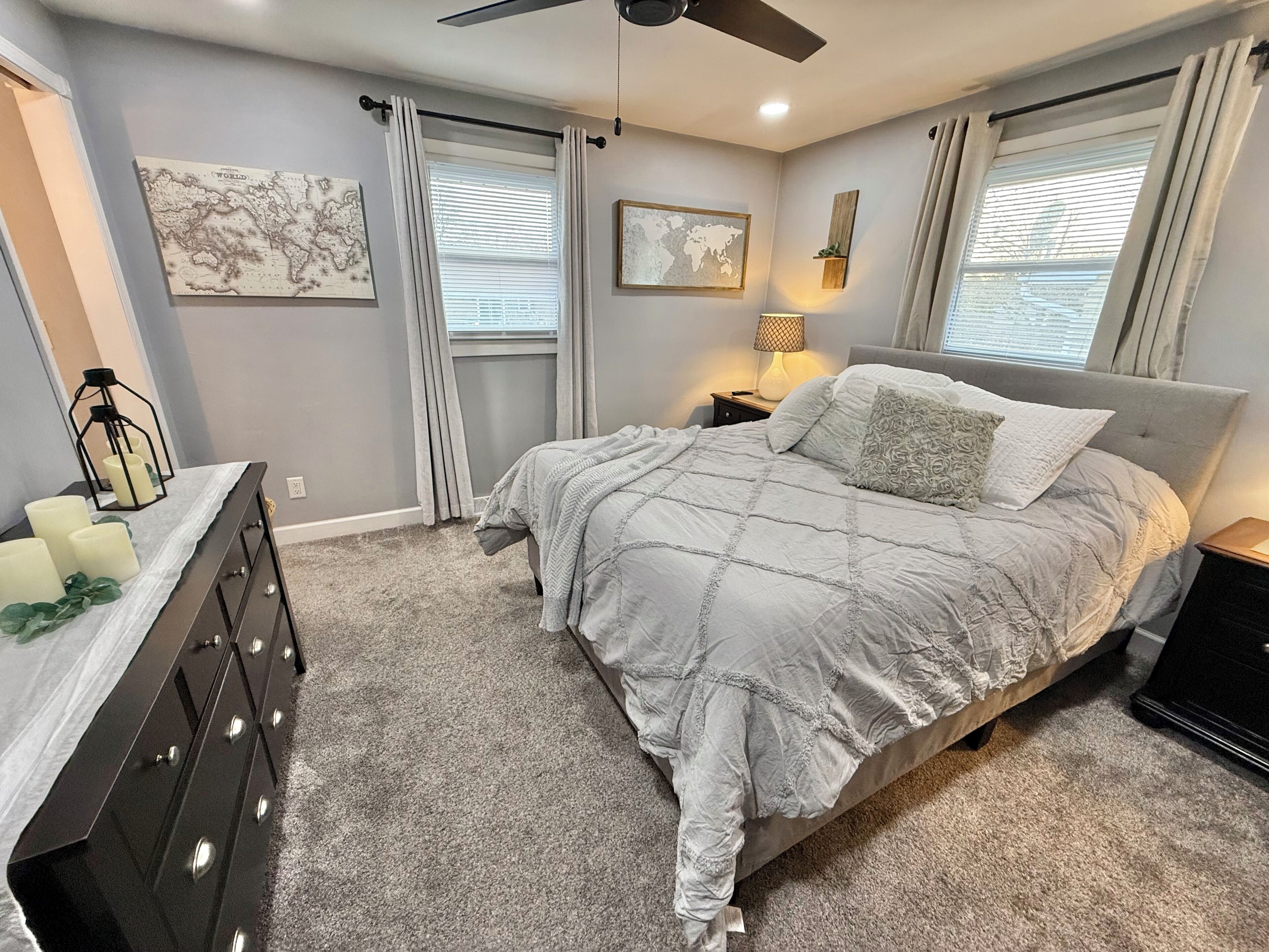 Une chambre à coucher avec un lit, une commode et deux fenêtres avec des rideaux.