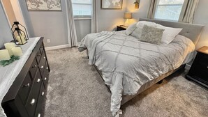 Une chambre à coucher avec un lit, une commode et deux fenêtres avec des rideaux.
