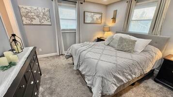 A bedroom with a bed, dresser, and two windows with curtains.