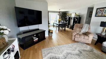 A living room with a flat-screen TV, a sofa, a coffee table, and a dining area with a table and chairs.
