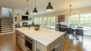 A spacious kitchen with a large island, modern pendant lights, and a dining area with a view.