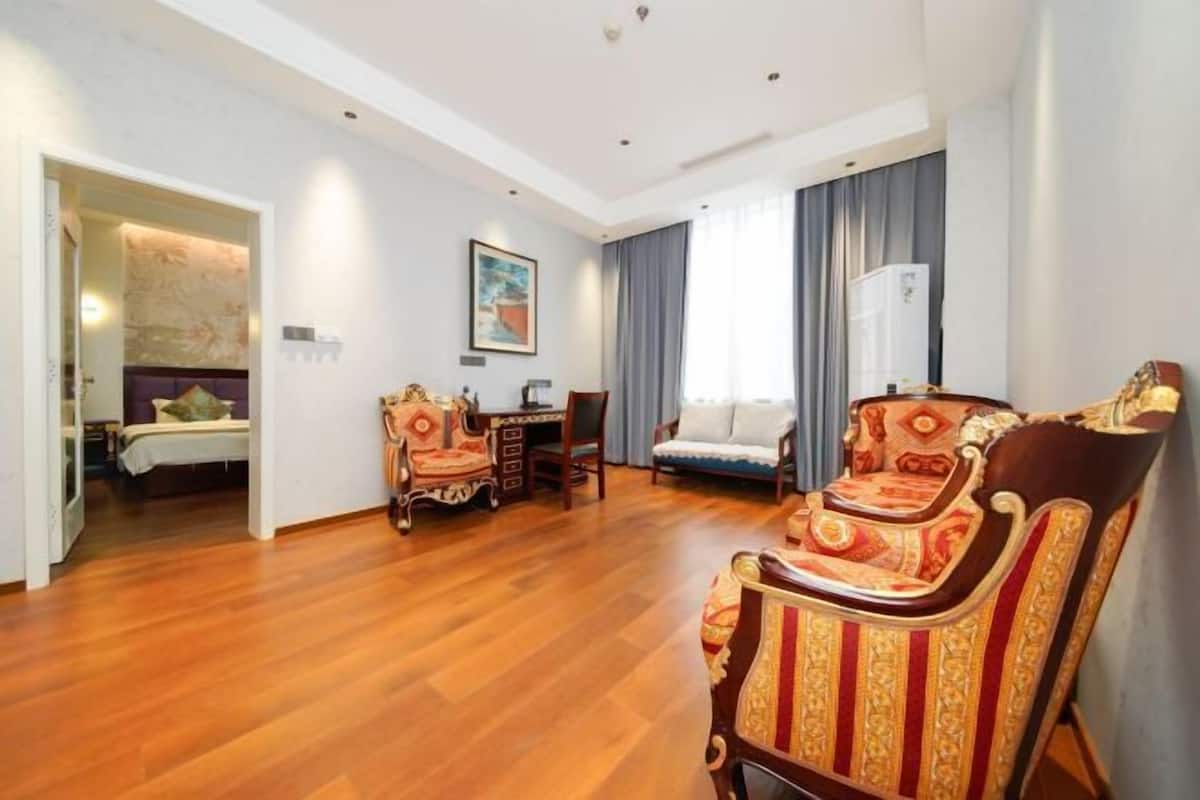 A spacious room with a wooden floor, a dining area with ornate chairs, a sofa, and a bed in the background.
