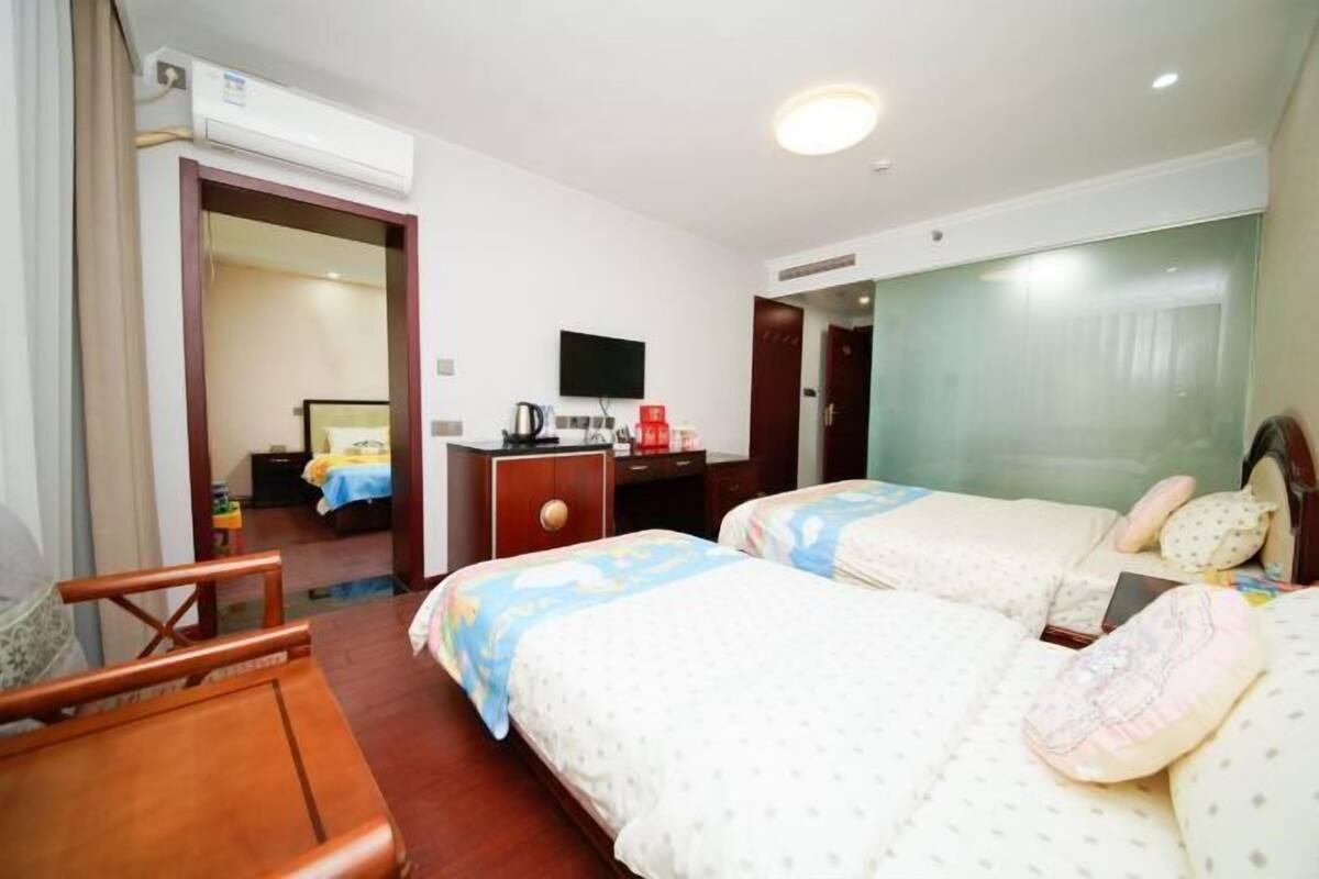 A hotel room with two beds, a desk, a chair, a television, and an air conditioning unit.