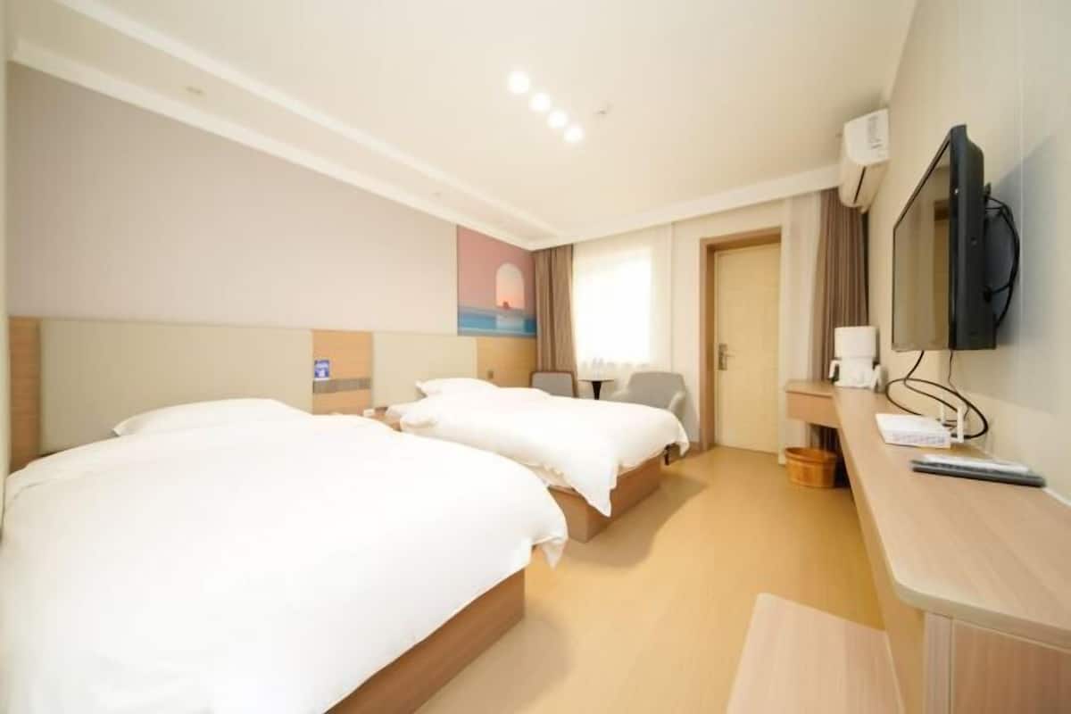A hotel room with two beds, a desk with a television, and a painting on the wall.