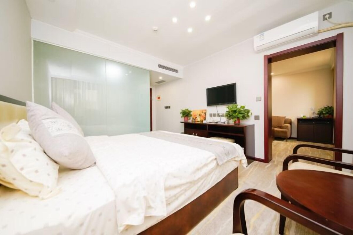 A hotel room with a bed, a desk, a chair, a TV, and a door leading to a sitting area.