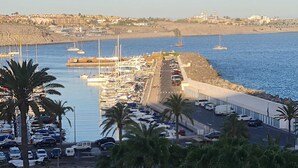 A marina with boats docked, a parking area, and a coastal town in the background.