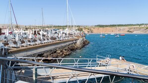 A marina with boats docked, a pier with lounge chairs, and a rocky shoreline in the background.