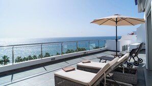 A rooftop terrace with lounge chairs, an umbrella, and a view of the ocean.