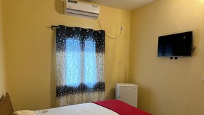 A bedroom with a bed, a TV mounted on the wall, and a small white appliance.