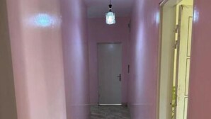A narrow hallway with pink walls and a tiled floor, leading to a door at the end.