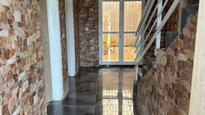 A hallway with stone walls and a shiny black tiled floor, leading to a door with a glass panel.