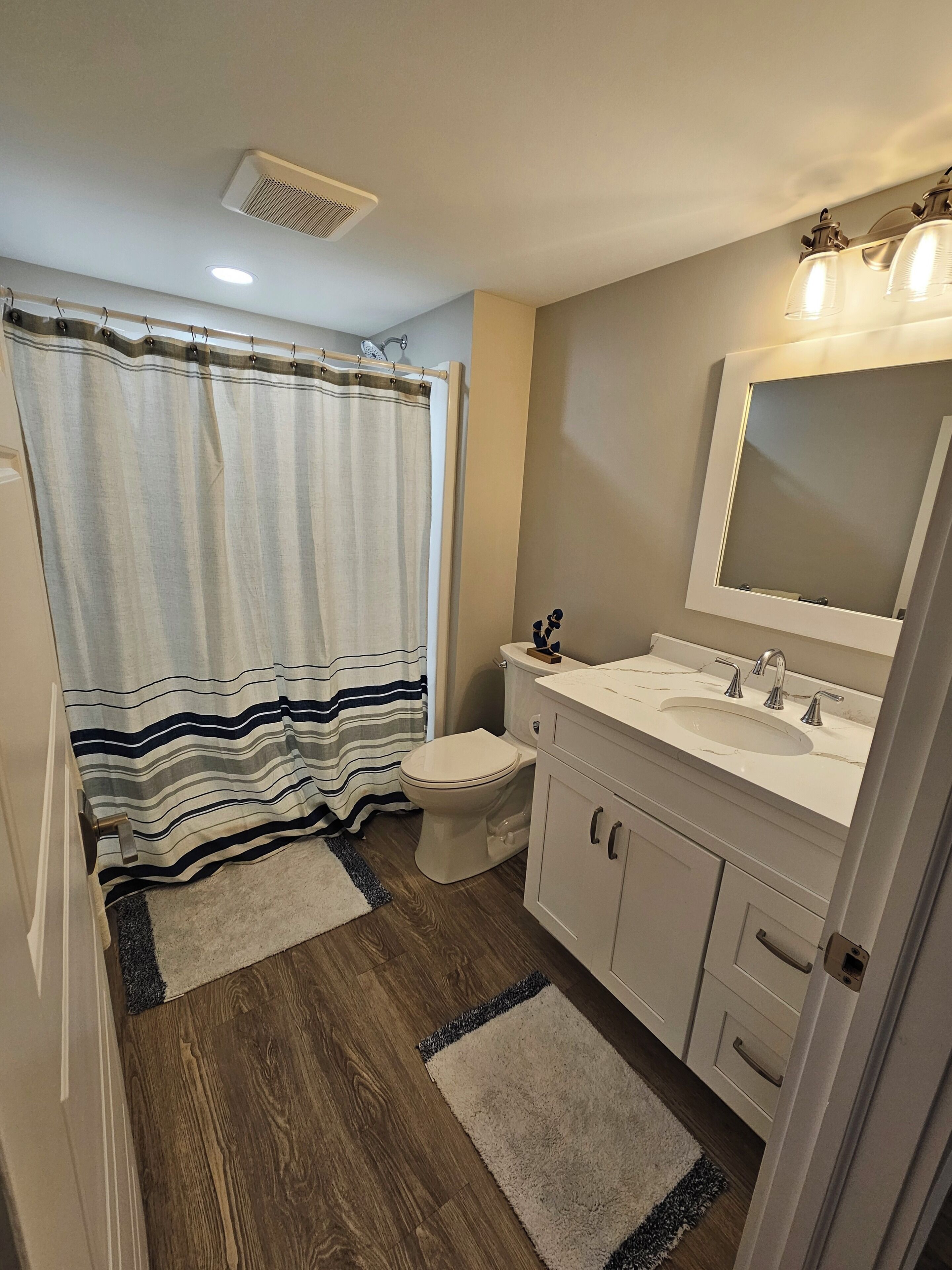 Une salle de bain avec un rideau de douche, des toilettes, un lavabo, un miroir et un plancher en bois.