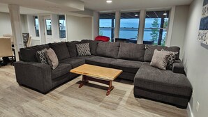Un salon moderne avec un canapé d’angle, une table basse en bois et de grandes fenêtres donnant sur l’extérieur.