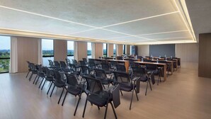 Ein geräumiger Konferenzraum mit hoher Decke, großen Fenstern und Reihen von Stühlen und Tischen.