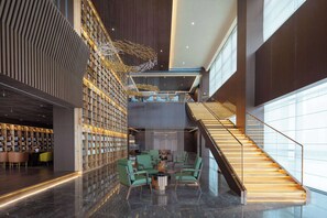 Un hall d’entrée moderne doté d’un escalier, d’un espace salon et d’un mur entier recouvert d’étagères à livres.