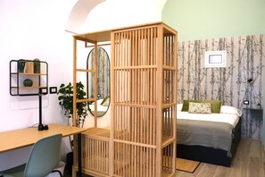 A bedroom with a bed, a desk with a chair, a wooden partition, a mirror, and a wall with a bamboo wallpaper pattern. - Homely Catania (Catania)