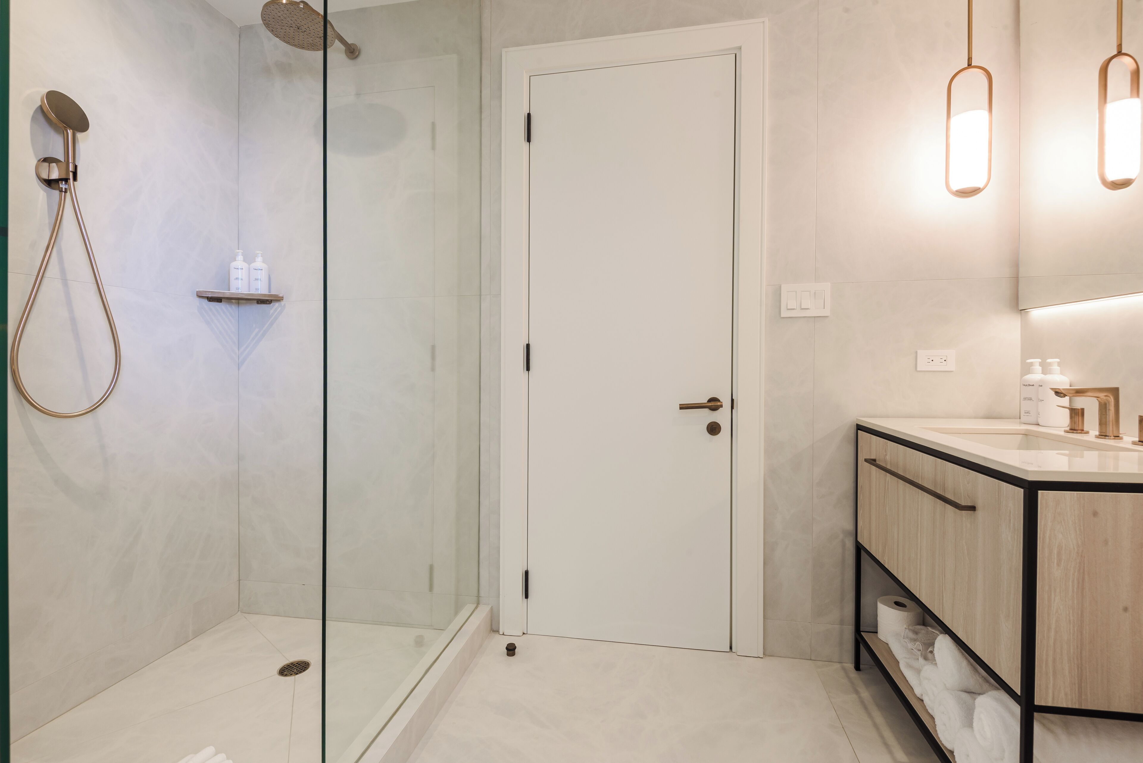 Un baño moderno con ducha envuelta en vidrio, una puerta blanca, un tocador con espejo y un perchero para toallas.