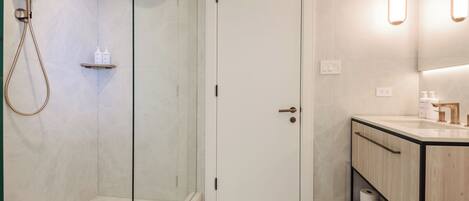 Un baño moderno con ducha envuelta en vidrio, una puerta blanca, un tocador con espejo y un perchero para toallas.