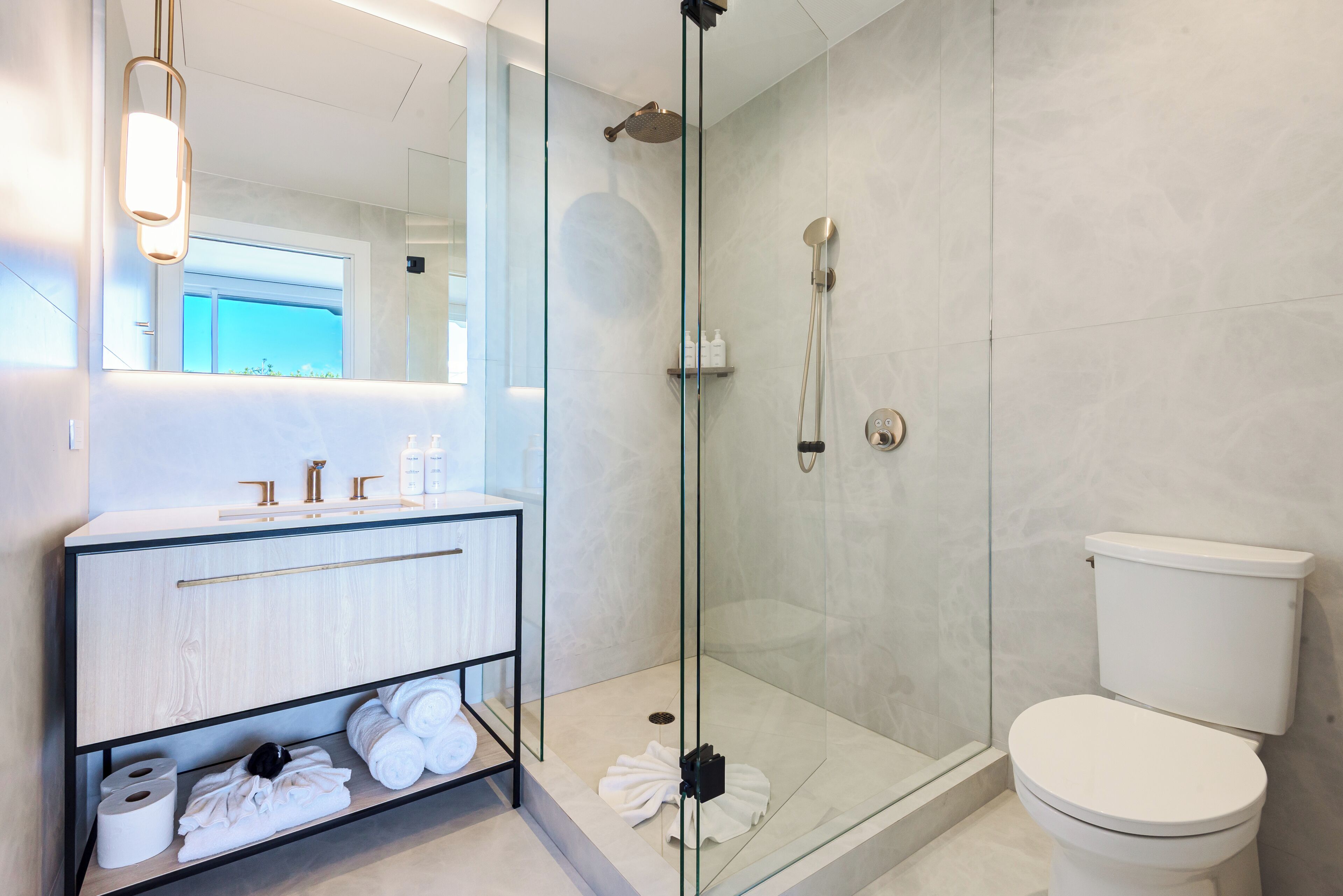 Un baño moderno con ducha envuelta en vidrio, inodoro blanco y tocador con espejo.