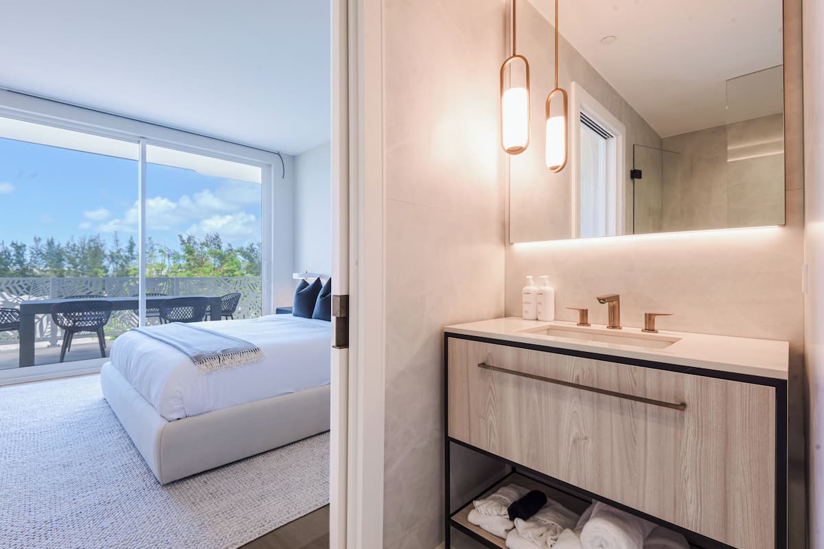 A modern bedroom with a large bed, a bathroom with a mirror, and a view of the outdoors.