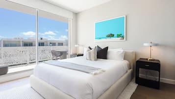 A modern bedroom with a large bed, a view of the sky, a framed picture, and a nightstand.