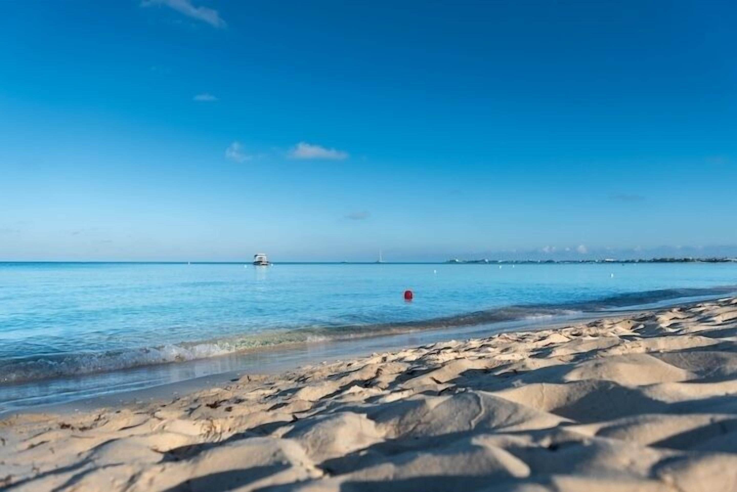 Ein Strand mit klarem, blauem Wasser, ein Boot in der Ferne und eine rote Boje.
