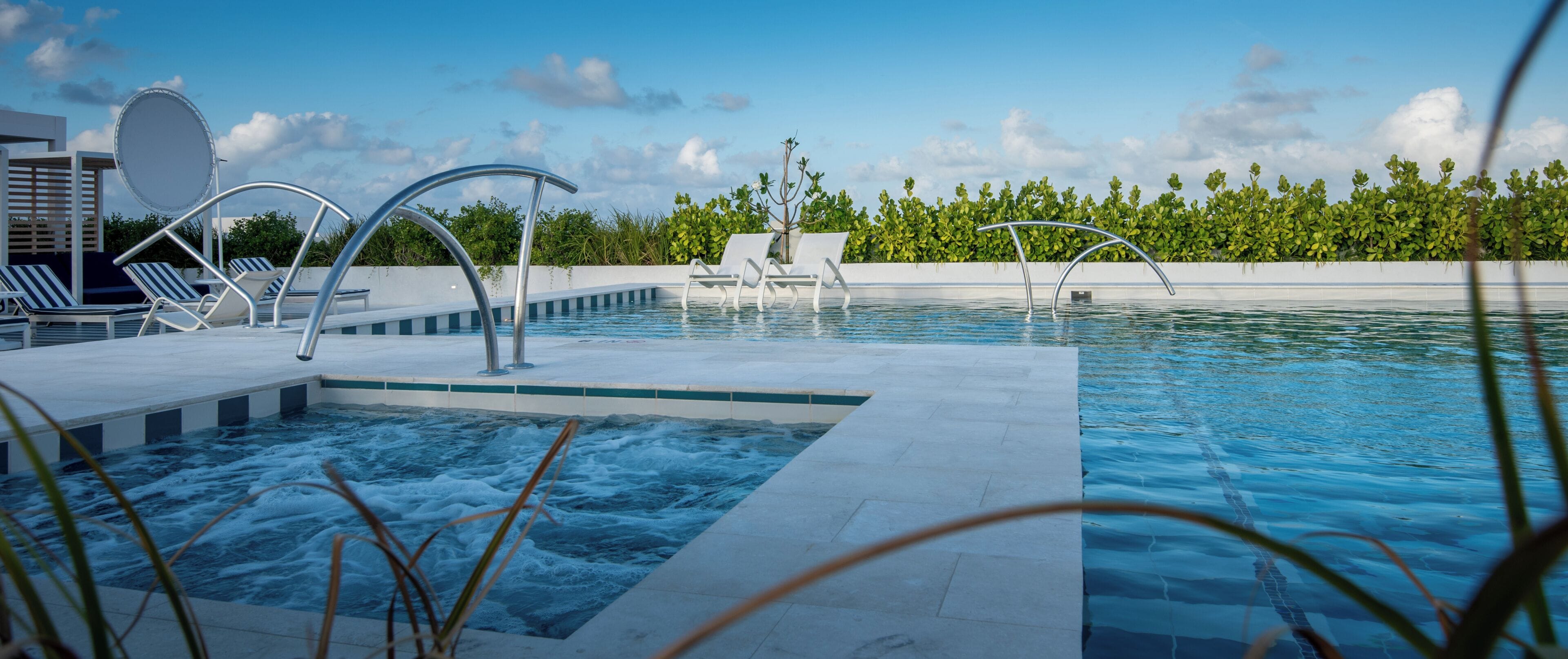 Un espace piscine avec des chaises longues, un jacuzzi et un ciel dégagé.