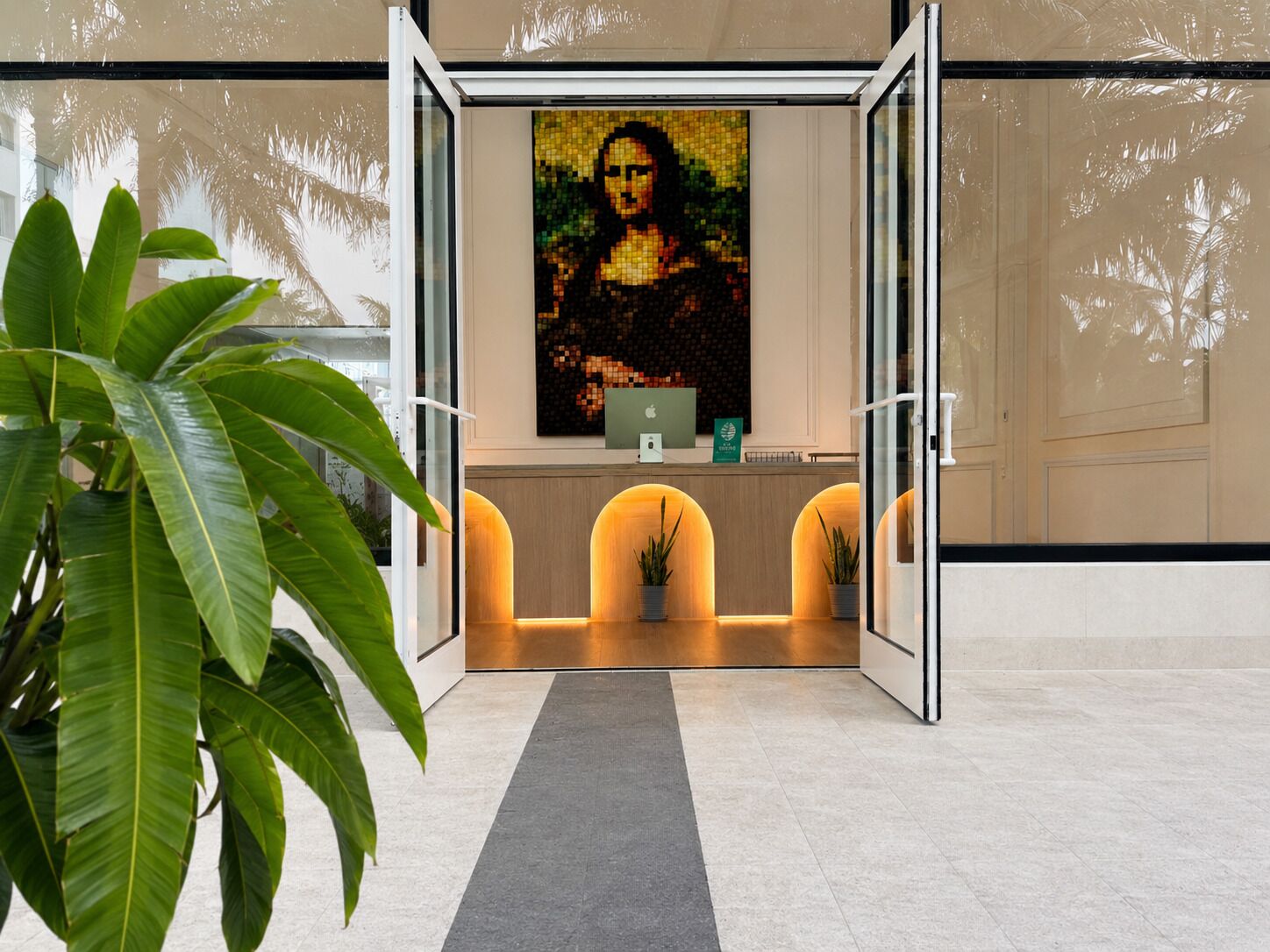 A reception area with a glass door, a large plant, and a wall-mounted artwork.