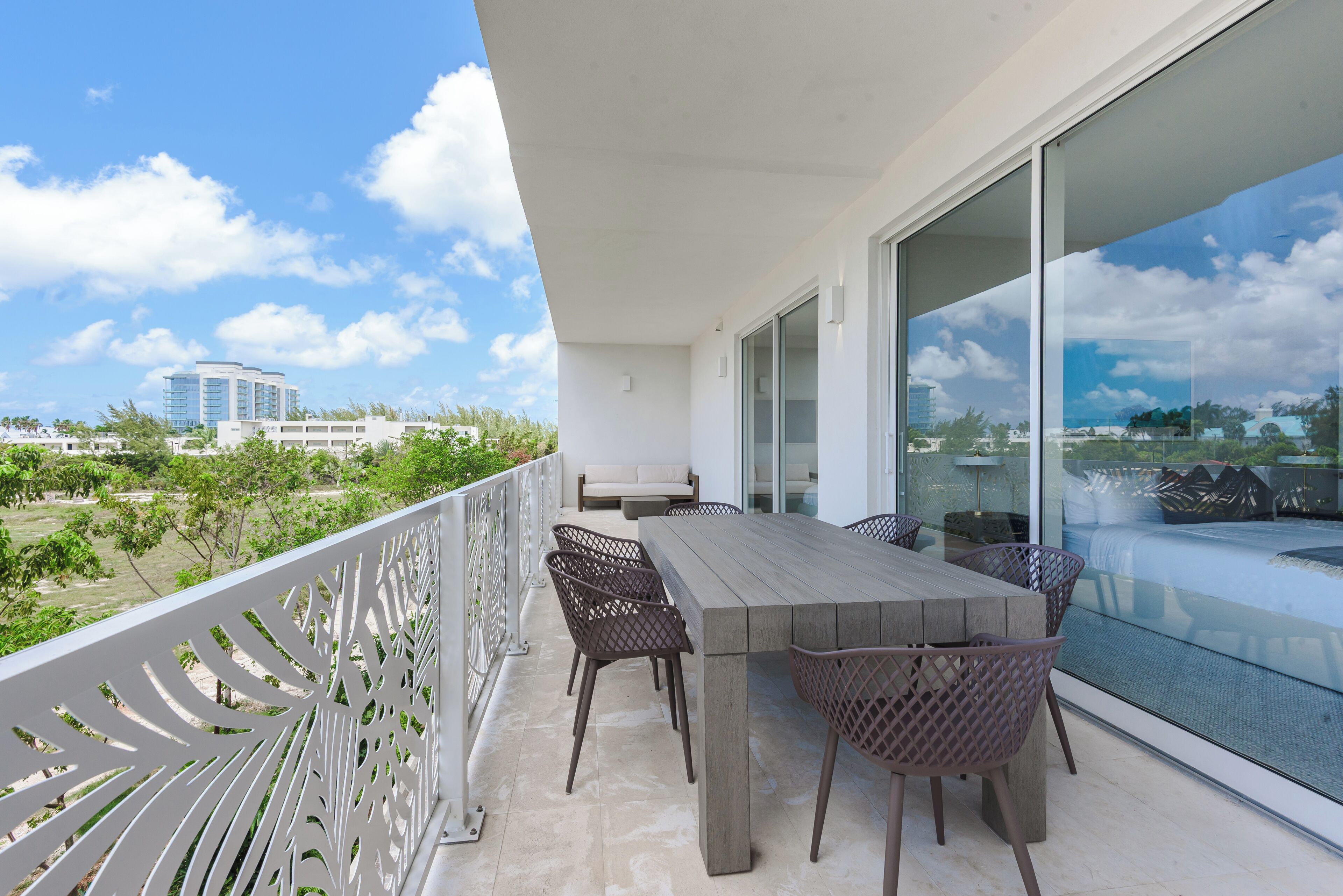 A balcony with a dining table and chairs, a sofa, and a view of a building and greenery.