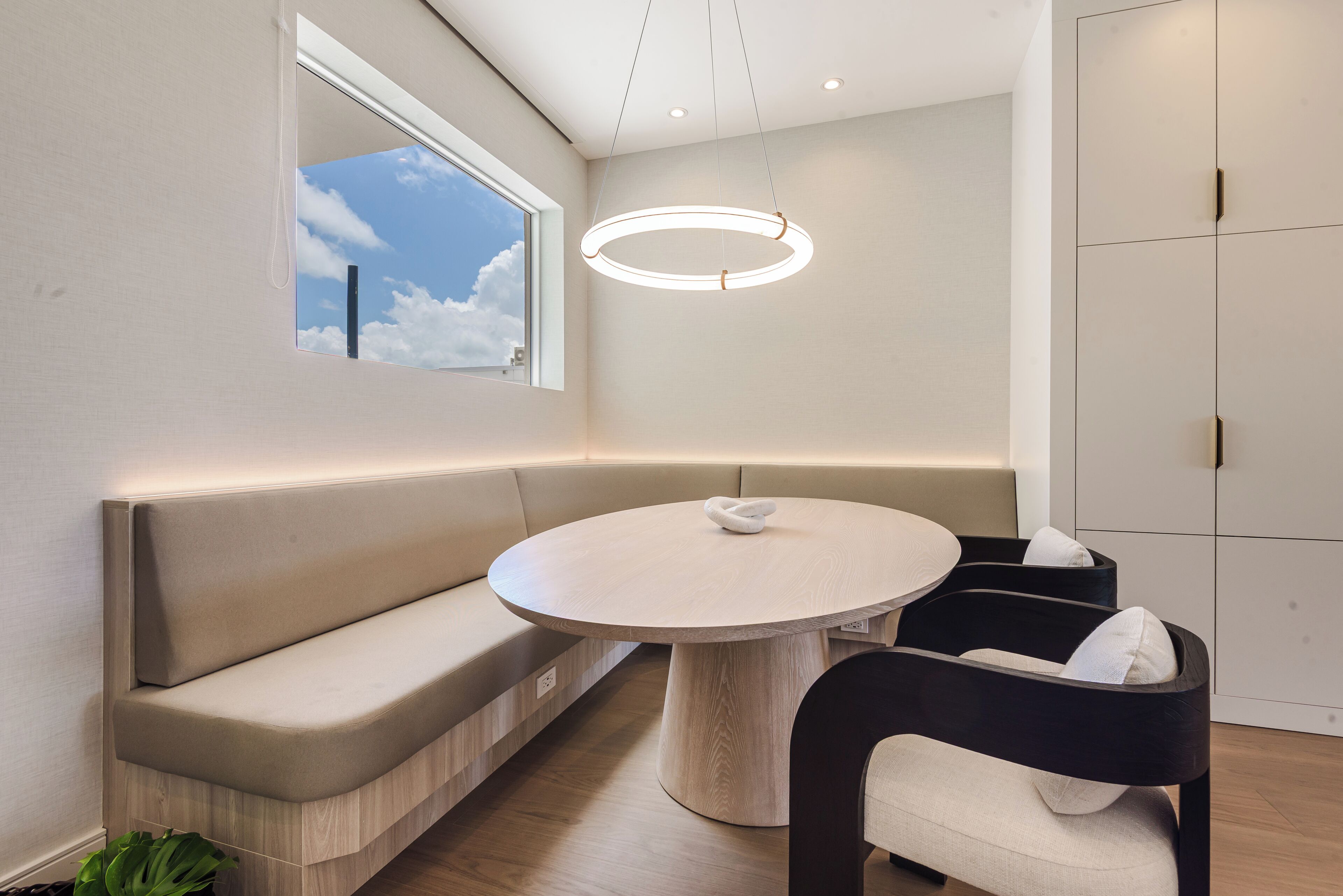 A modern room with a round table, bench seating, a window with a view, and a pendant light.