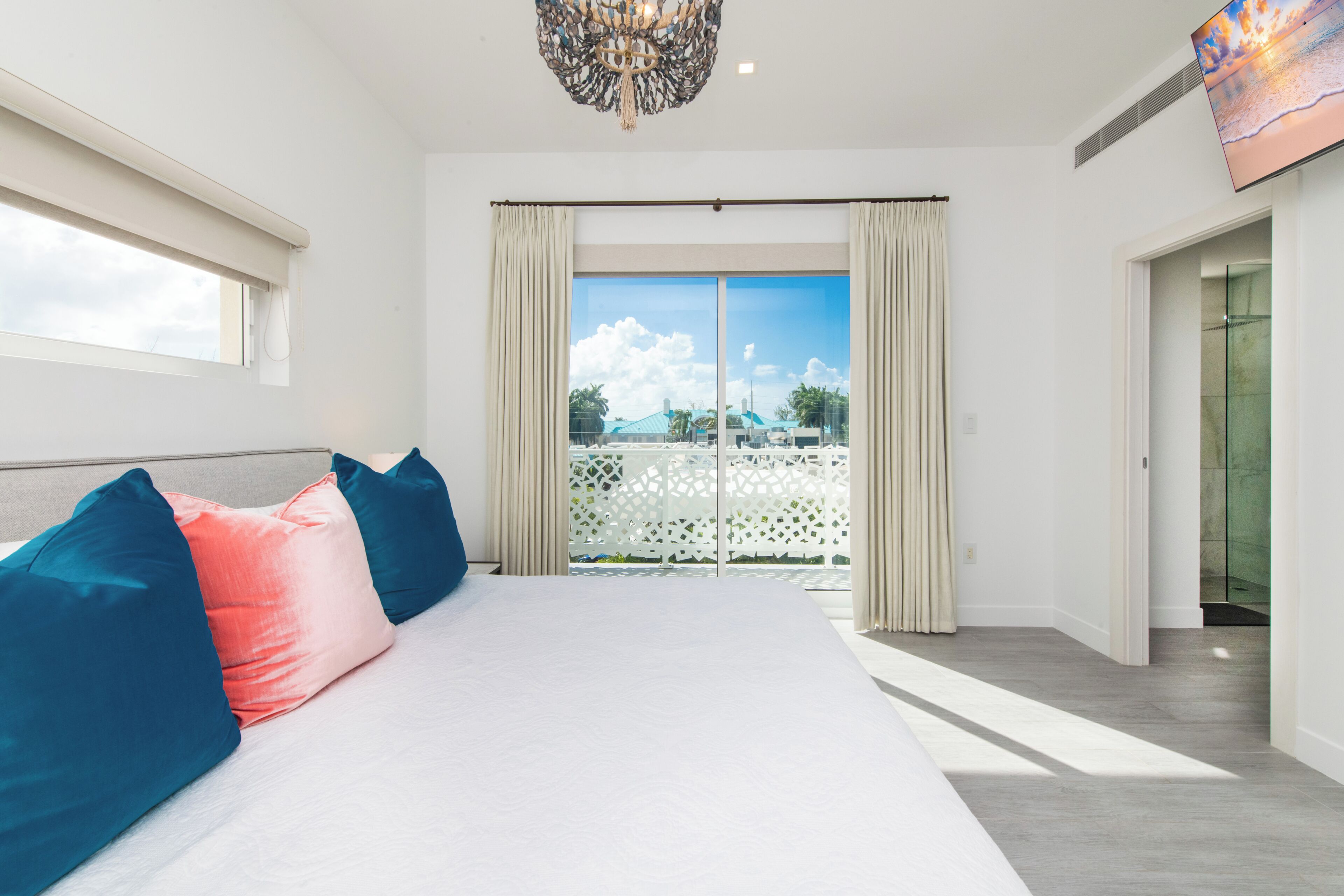 A bedroom with a large bed, a chandelier, a sliding glass door to a balcony, and a view of the outdoors.