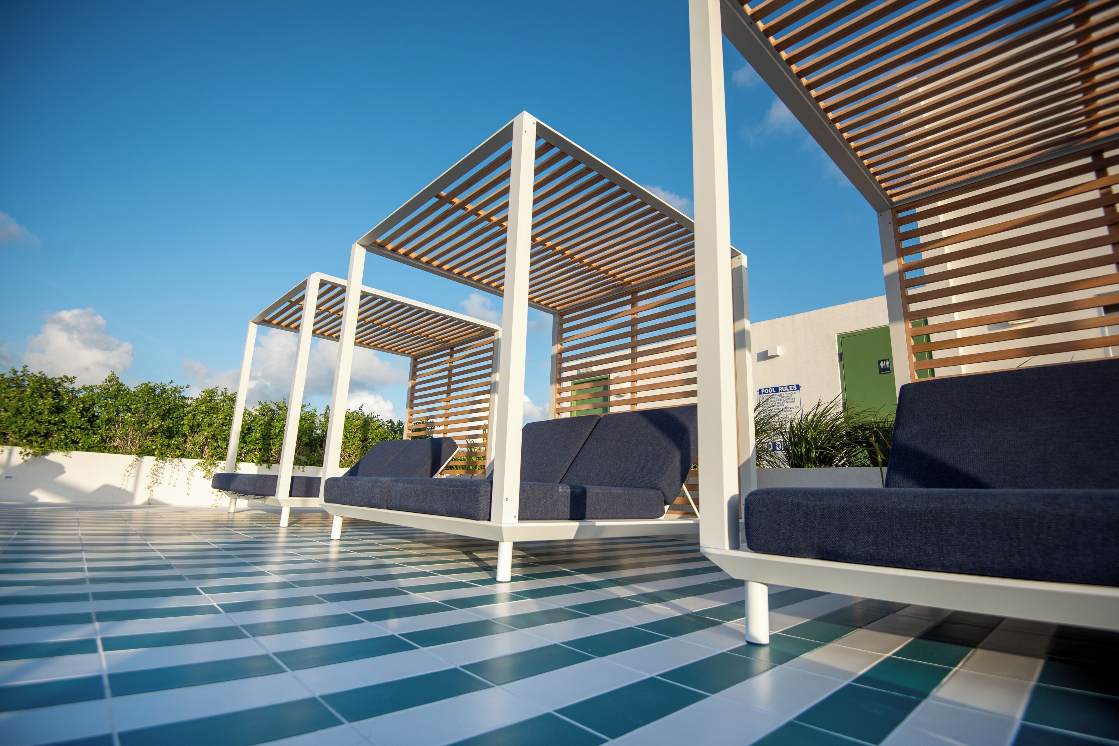 Terrasse mit kariertem Boden, einer grünen Tür und einem Schild mit der Aufschrift 'POOL RULES'.