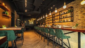 A bar area with wooden floors, green upholstered chairs, and a brick wall with shelves of bottles. - The Grove (Seven Mile Beach)