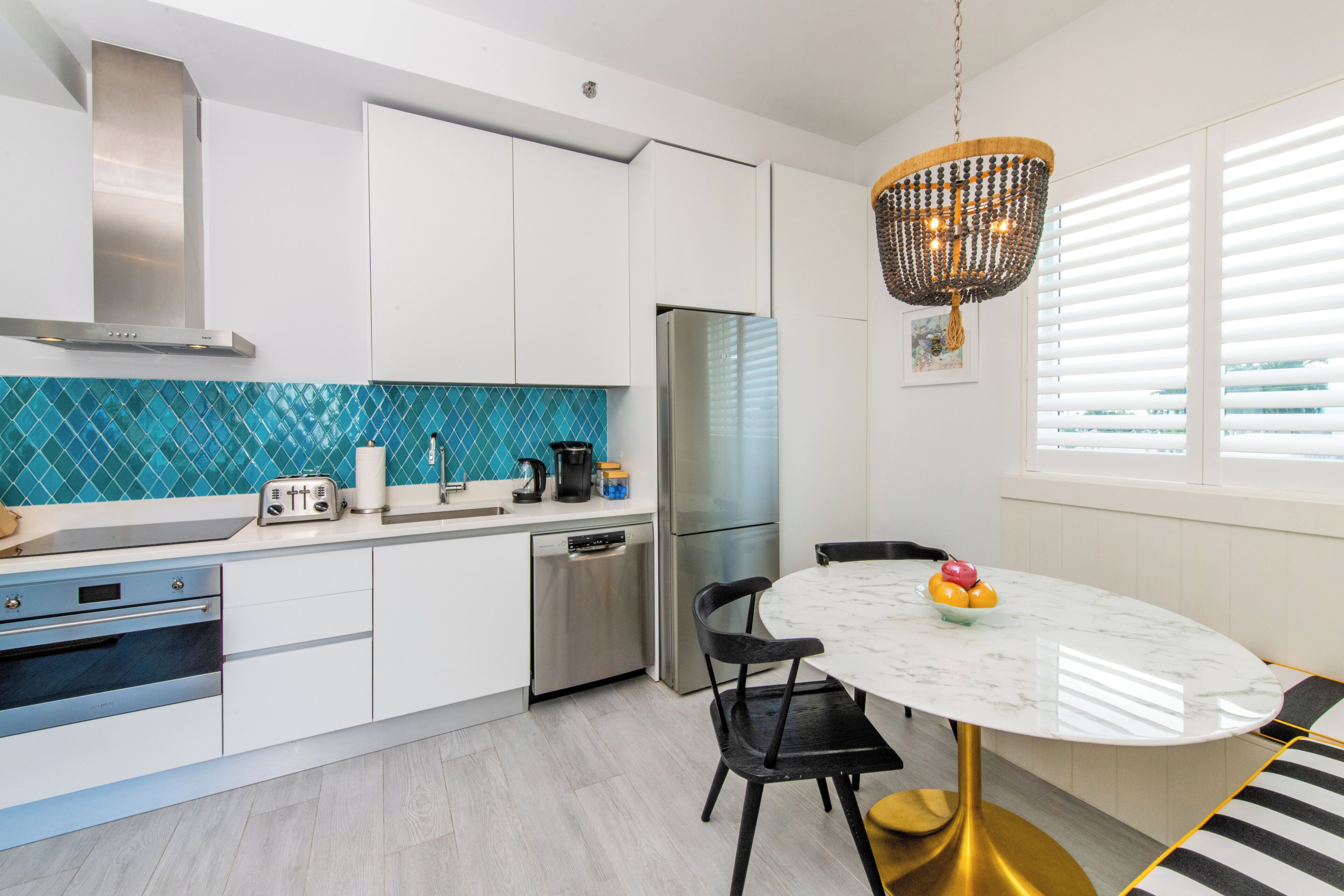 A modern kitchen with white cabinets, a stainless steel refrigerator, a blue tiled backsplash, and a round table with chairs.