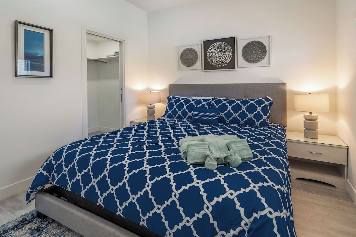 A bedroom with a patterned bedspread, bedside lamps, a mirror, and artwork on the wall.