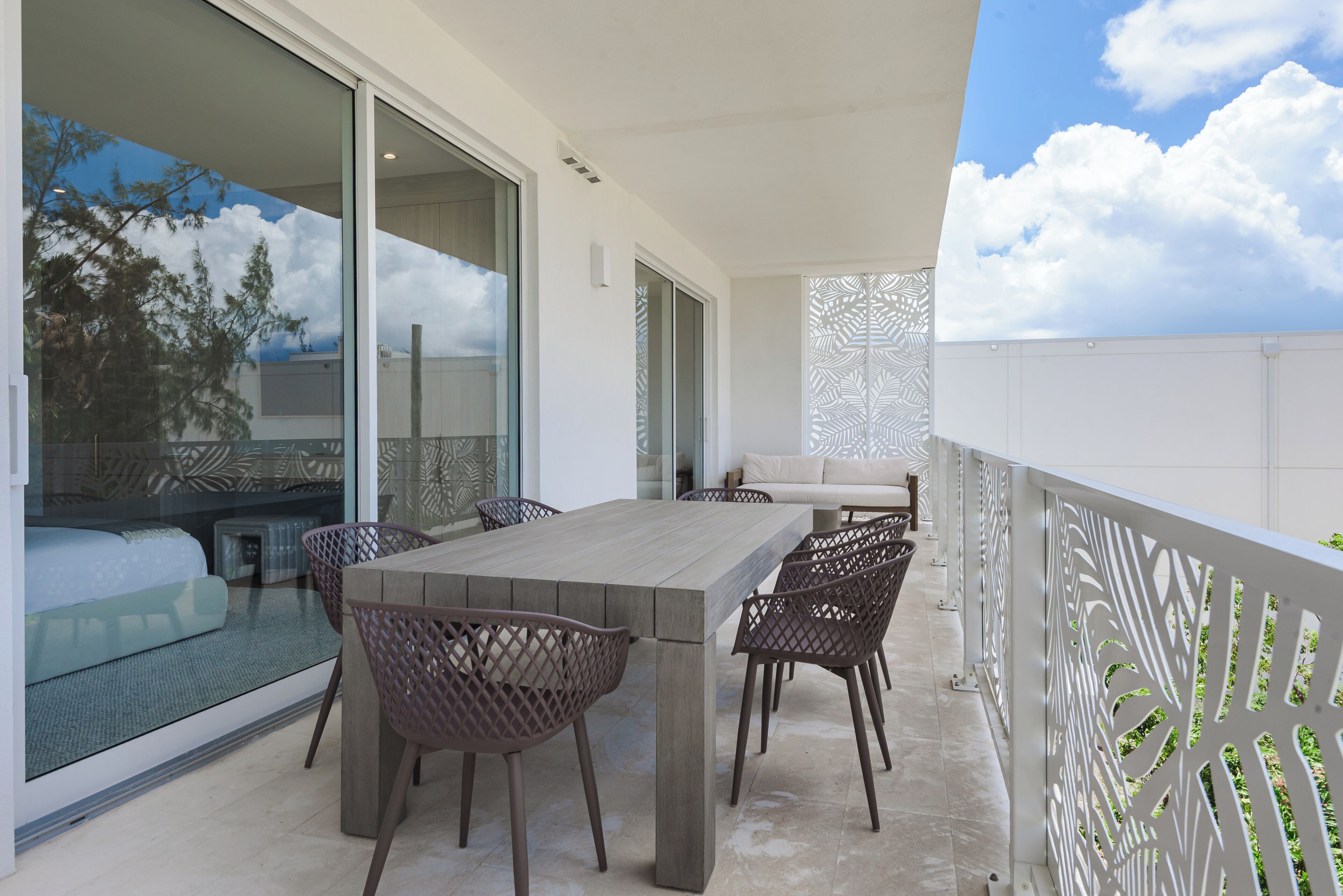 A balcony with a dining table and chairs, a sofa, and a patterned wall.