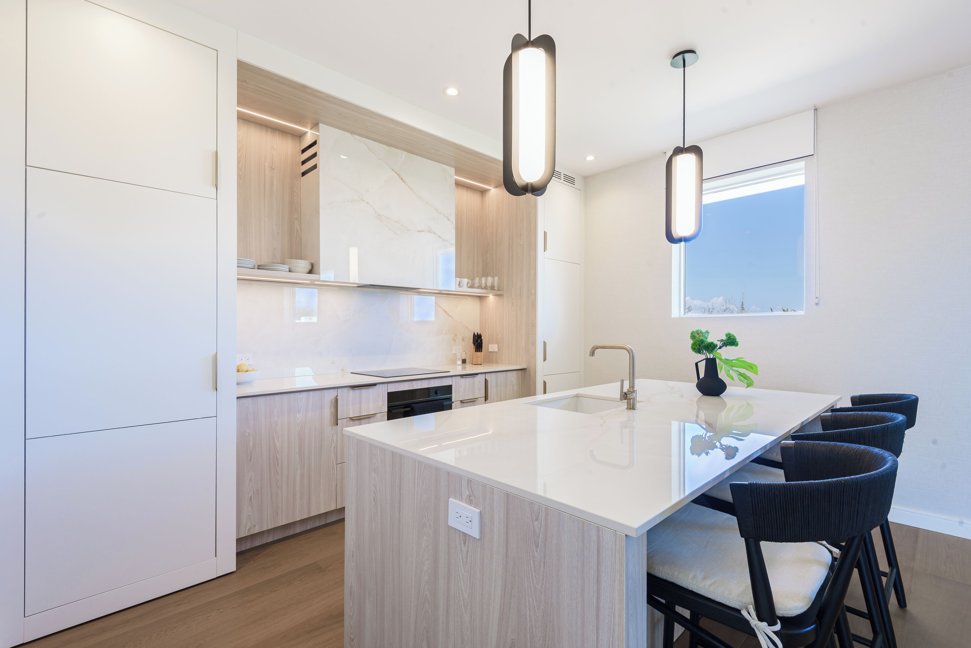Una cucina moderna con isola centrale, mobili bianchi e illuminazione a sospensione.