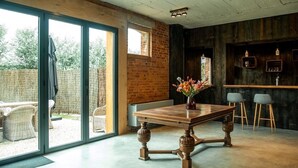 A dining area with a wooden table and chairs, a vase with flowers, and a view through large sliding doors to an outdoor patio with wicker furniture.