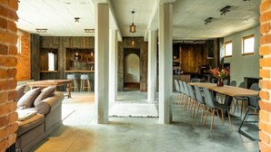 A spacious, open-plan living area with a long dining table and multiple chairs, a sofa, and a kitchen in the background.