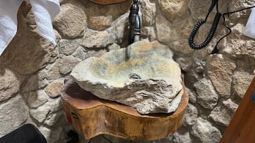 Uma pia de pedra rústica com uma bacia de madeira, um espelho e um telefone.
