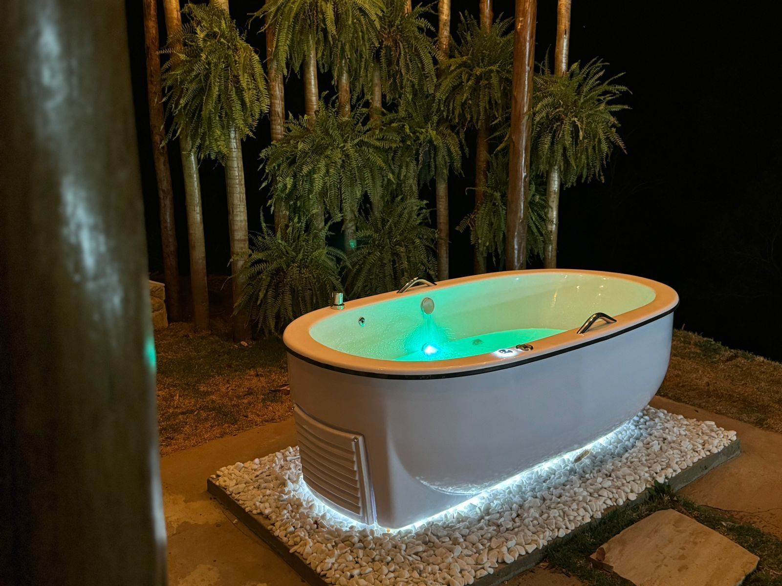 Tinaja exterior con interior iluminado, rodeada de guijarros blancos y palmeras.