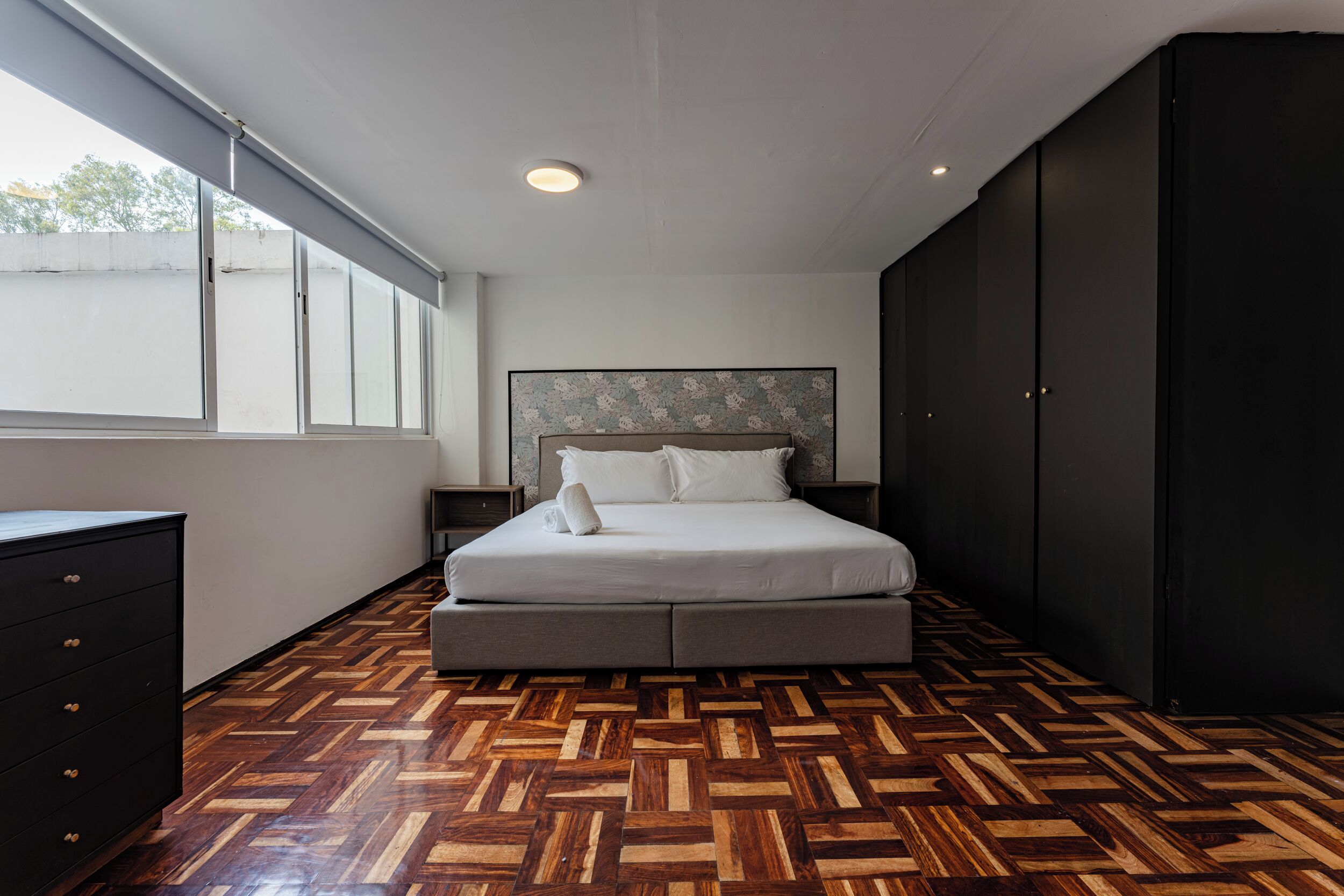 A bedroom with a large bed, a dresser, a nightstand, and a wardrobe.