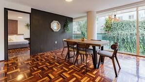 A modern interior with a dining area, a bed, and a view of greenery outside.