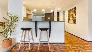 A modern kitchen with two bar stools, a potted plant, and a wooden floor.