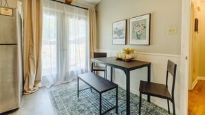 A dining area with a table, chairs, and a bench. There is a refrigerator and a window with curtains.