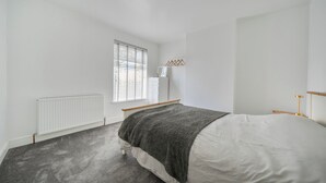 Une chambre à coucher avec un lit, un radiateur, une fenêtre avec des stores et une table de chevet.