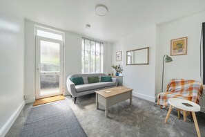 Un salon avec un canapé, une table basse et un fauteuil recouvert d’une couverture.