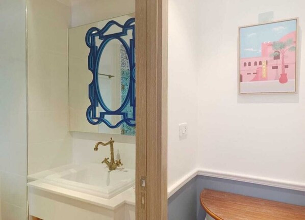 Une salle de bain avec un lavabo blanc, un miroir à cadre bleu et un tableau encadré accroché au mur.
