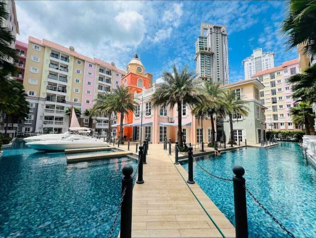 A hotel pool area with a clear view of the pool, a palm tree-lined pathway, and colorful buildings in the background.